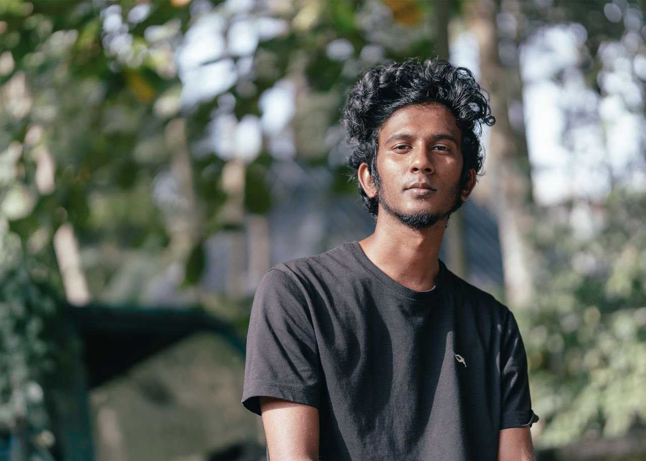 Portrait of a young man with curly hair wearing a black shirt, outdoors in natural light.