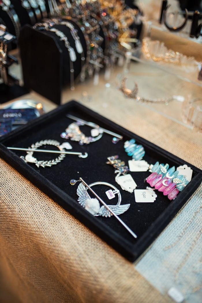 Assorted jewelry on display in a black tray over a burlap cloth at a market.