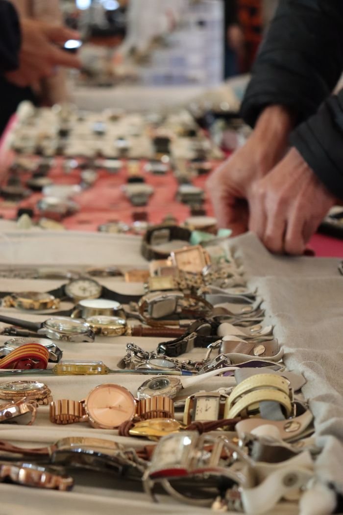 A detailed view of various vintage watches displayed on a market stall, hands adjusting the collection.
